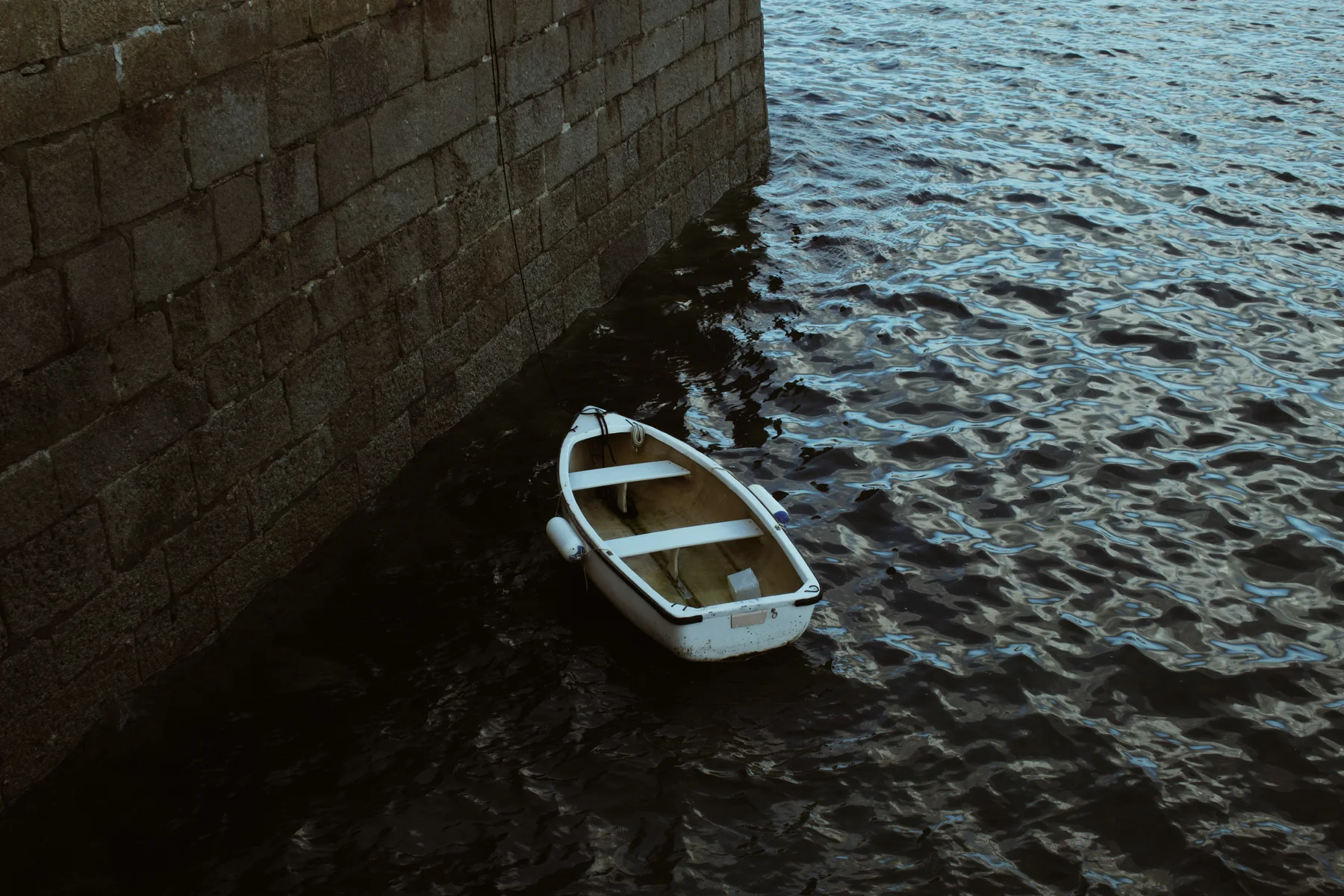 Small white boat beside a dark stone wall